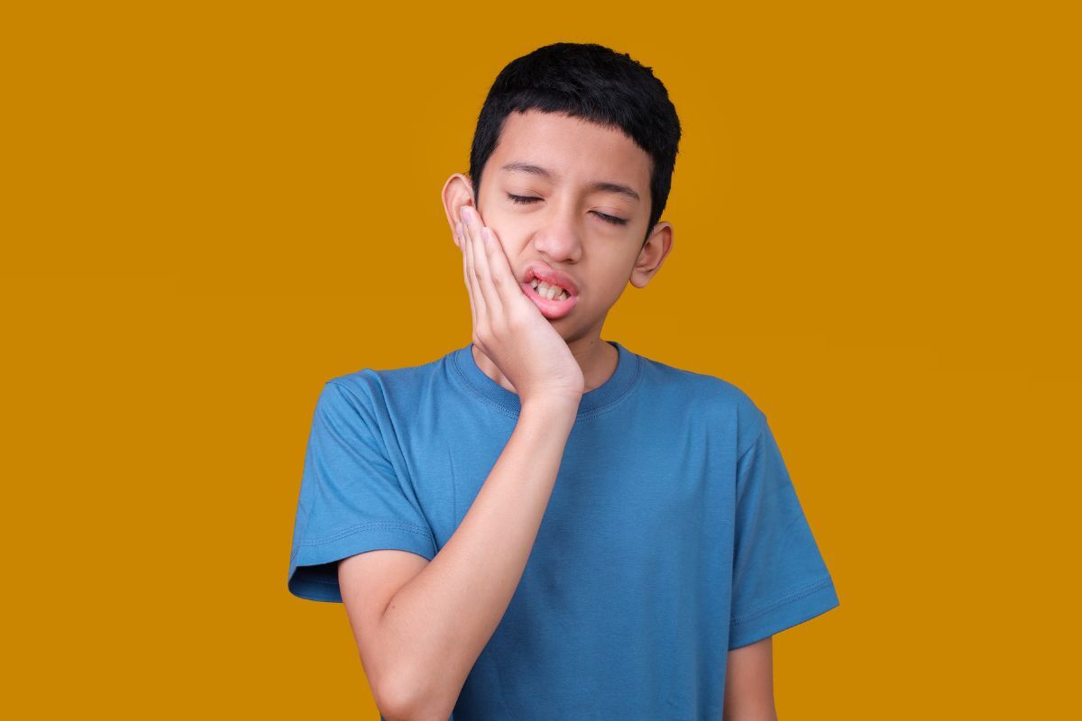 Boy holding his cheek in pain, illustrating TMJ discomfort in children.
