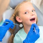 Young girl receiving dental examination in chair with dentist using mirror and explorer tool.