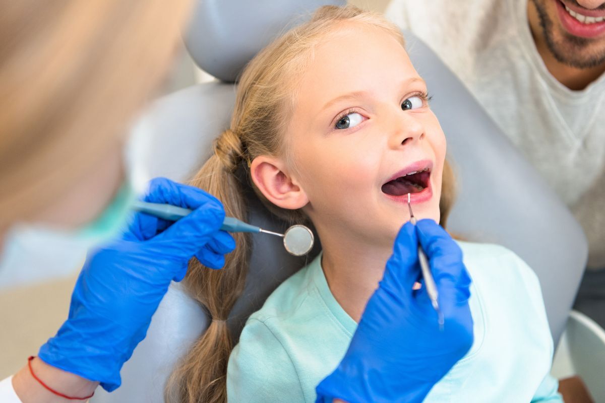 Young girl receiving dental examination in chair with dentist using mirror and explorer tool.