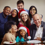 Happy multi-generational family celebrating Christmas together with Santa hats and festive meal.