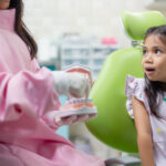 Young patient in dental chair smiles as dentist explains orthodontic treatment during consultation.