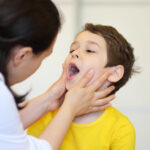 Pediatric dentist examining child's open mouth during oral health assessment.
