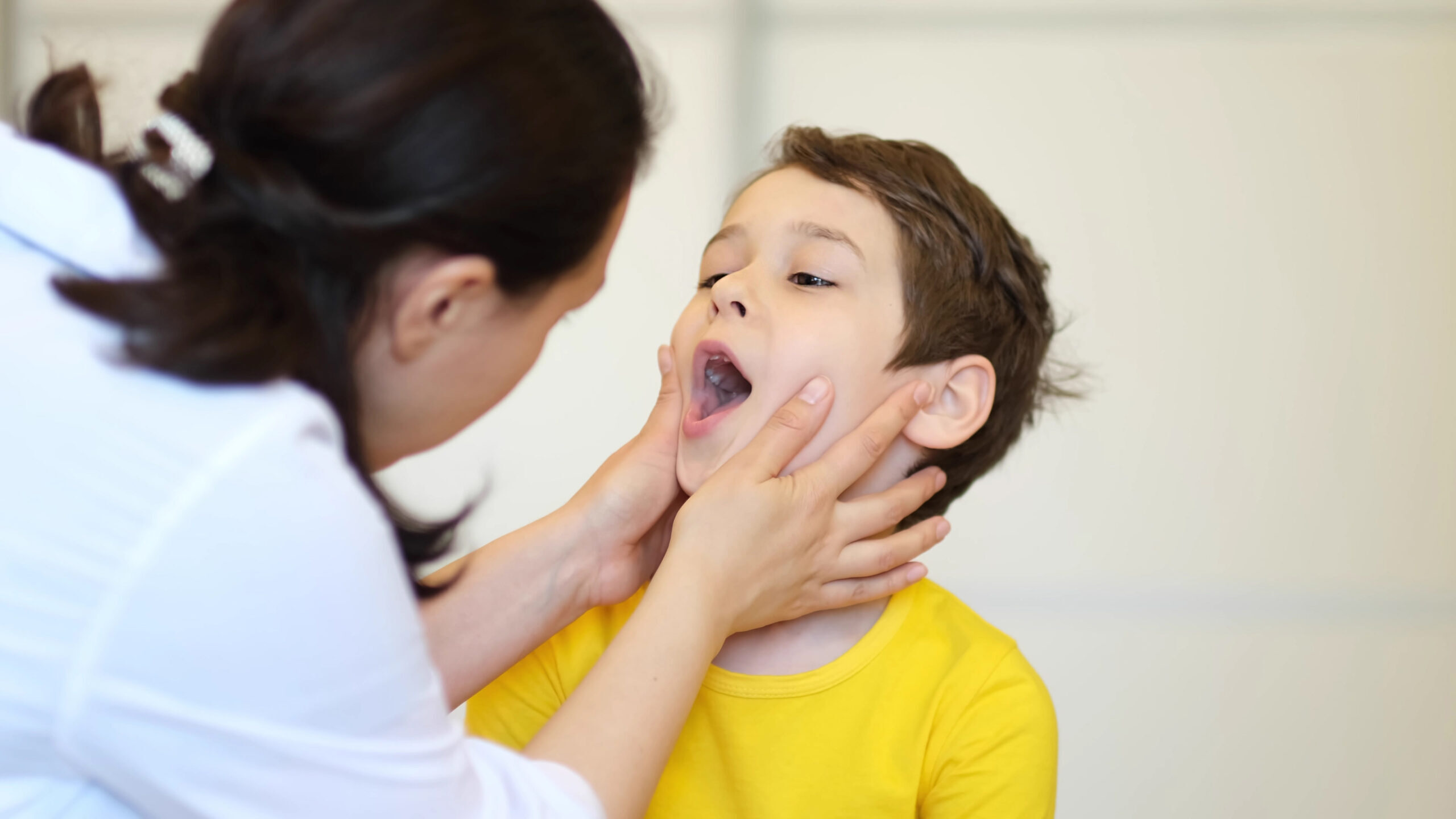 Pediatric dentist examining child's open mouth during oral health assessment.