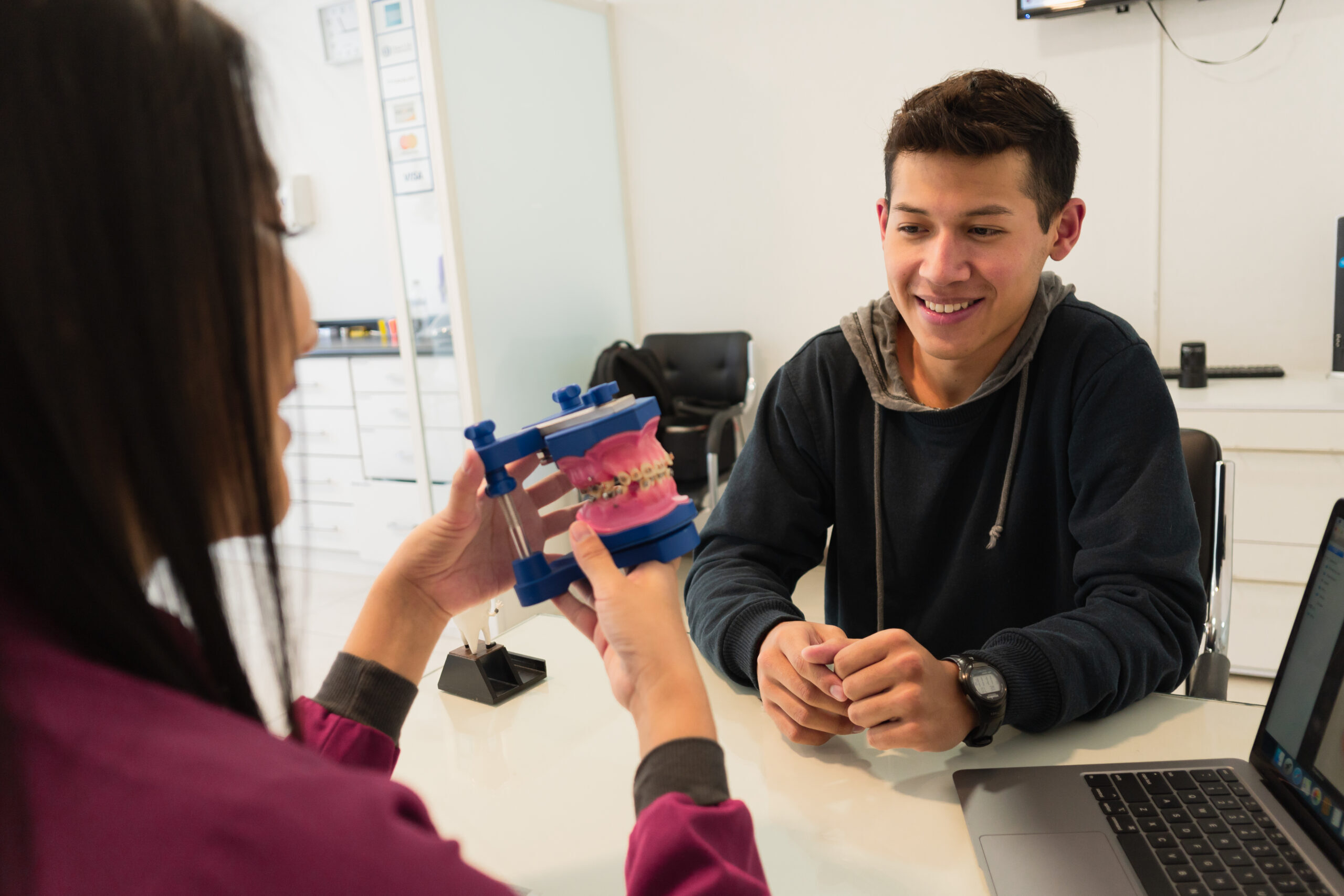 Young teen patient examining dental model with orthodontist during consultation.