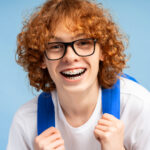 Happy teen with braces smiling while wearing a blue backpack in dental care setting.