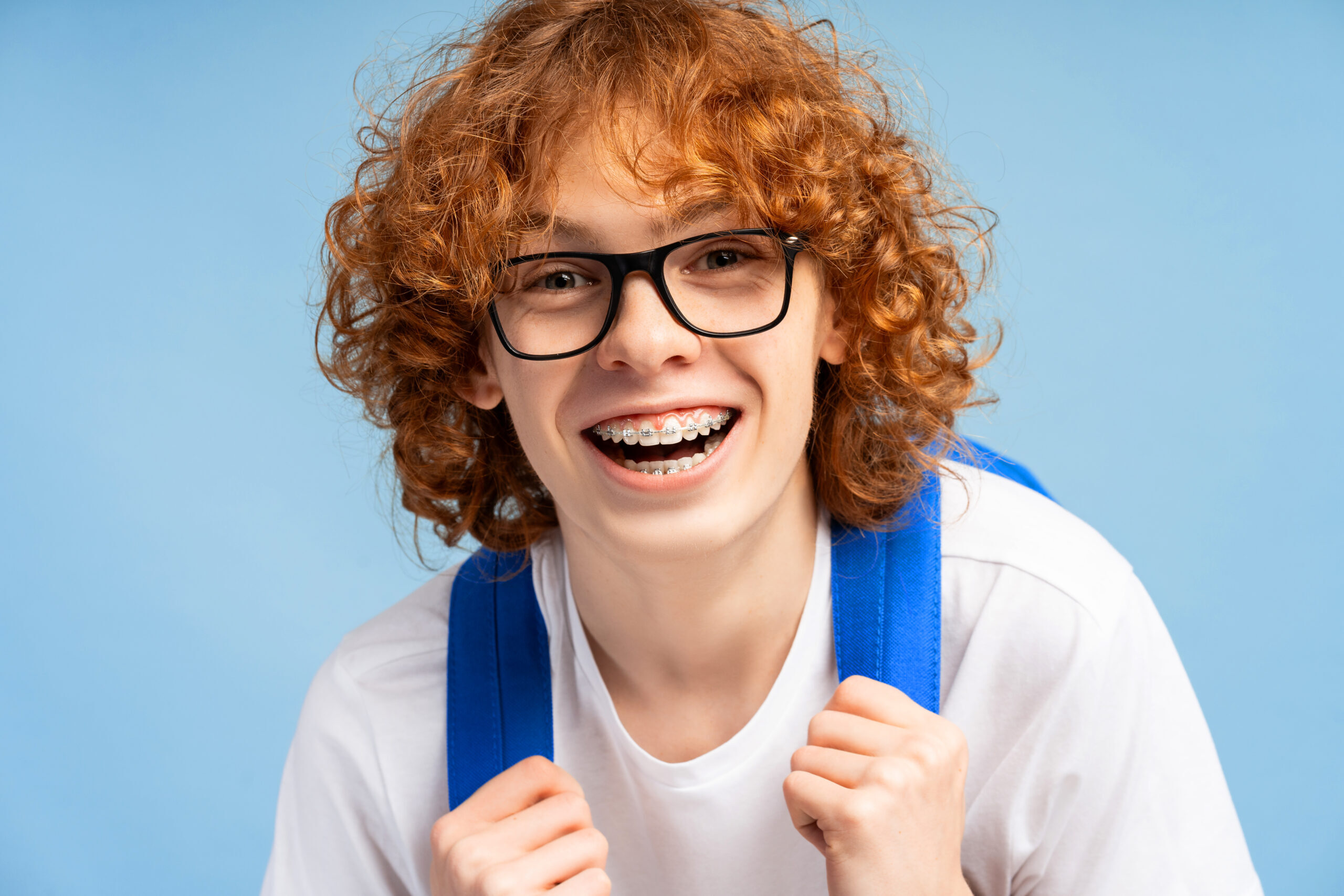 Happy teen with braces smiling while wearing a blue backpack in dental care setting.