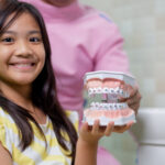 Young patient holding orthodontic model showing colorful braces treatment options in dental office.