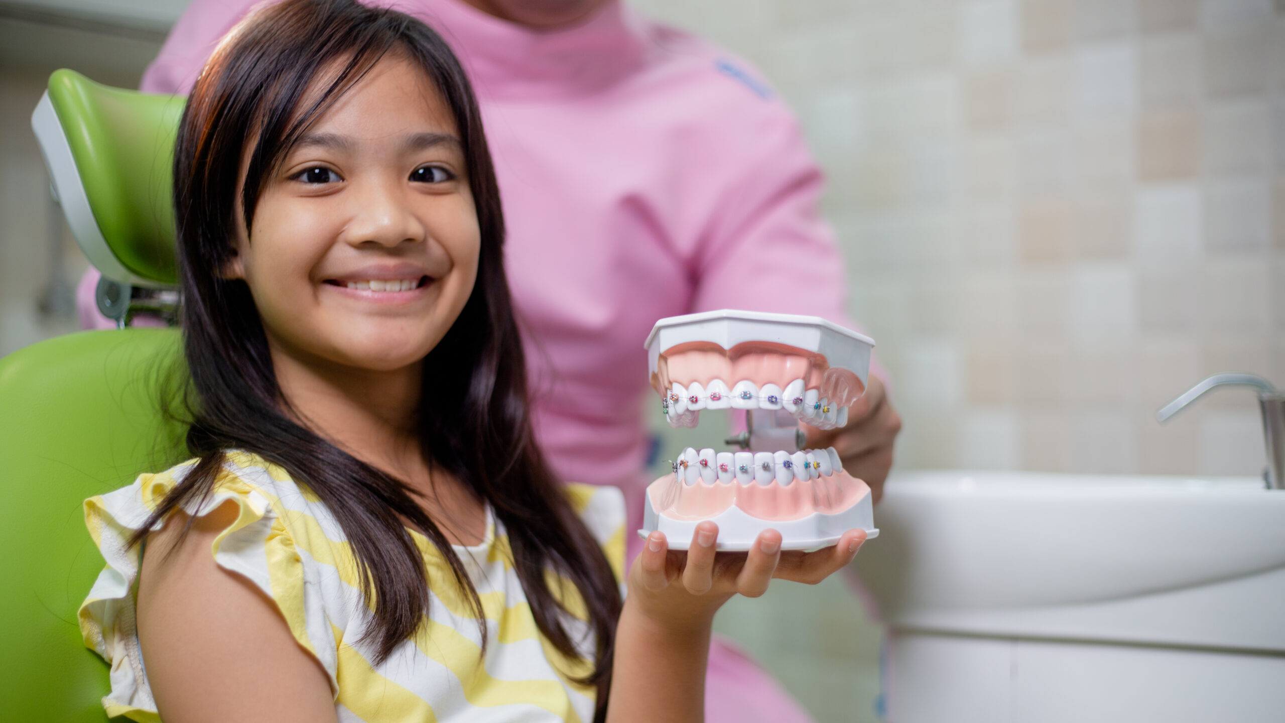 Young patient holding orthodontic model showing colorful braces treatment options in dental office.