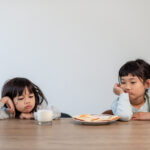 Two young girls looking upset while sitting at a table with milk and food, illustrating child tooth pain.