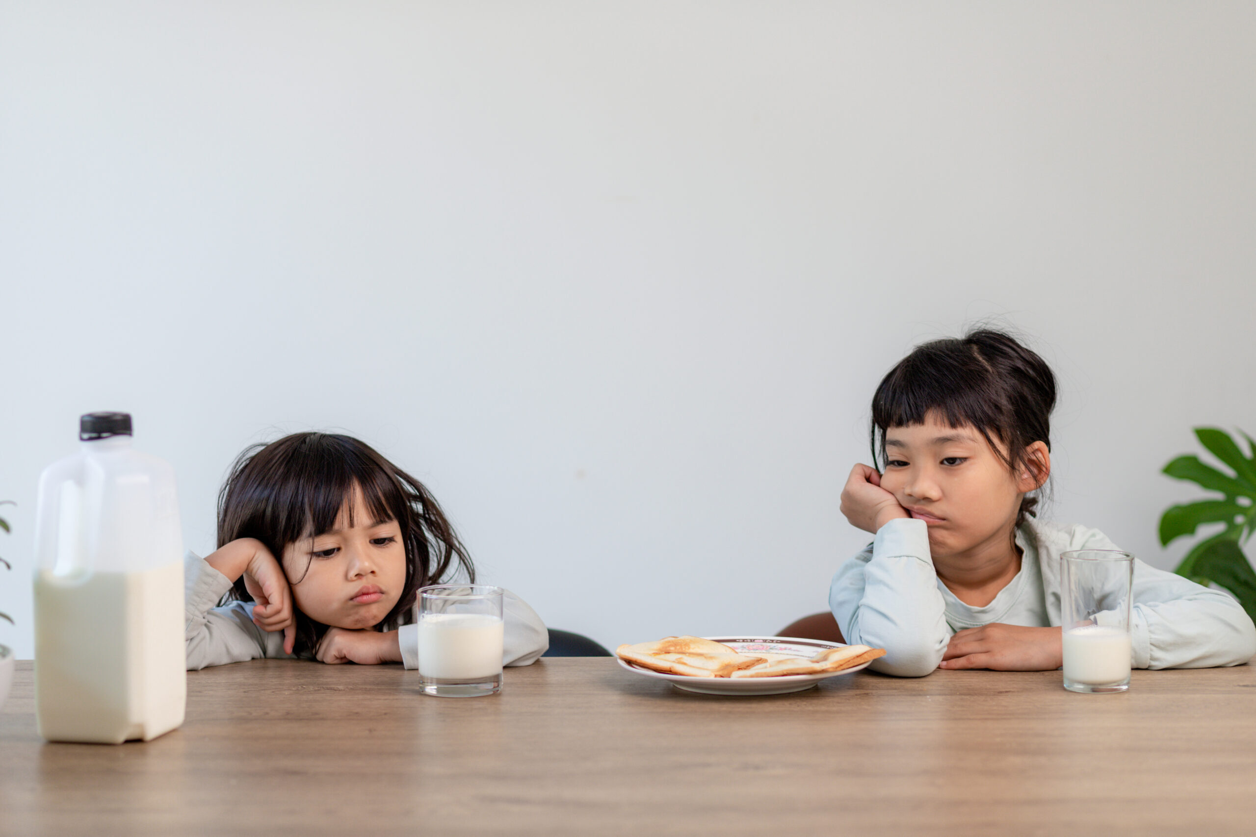 Two young girls looking upset while sitting at a table with milk and food, illustrating child tooth pain.