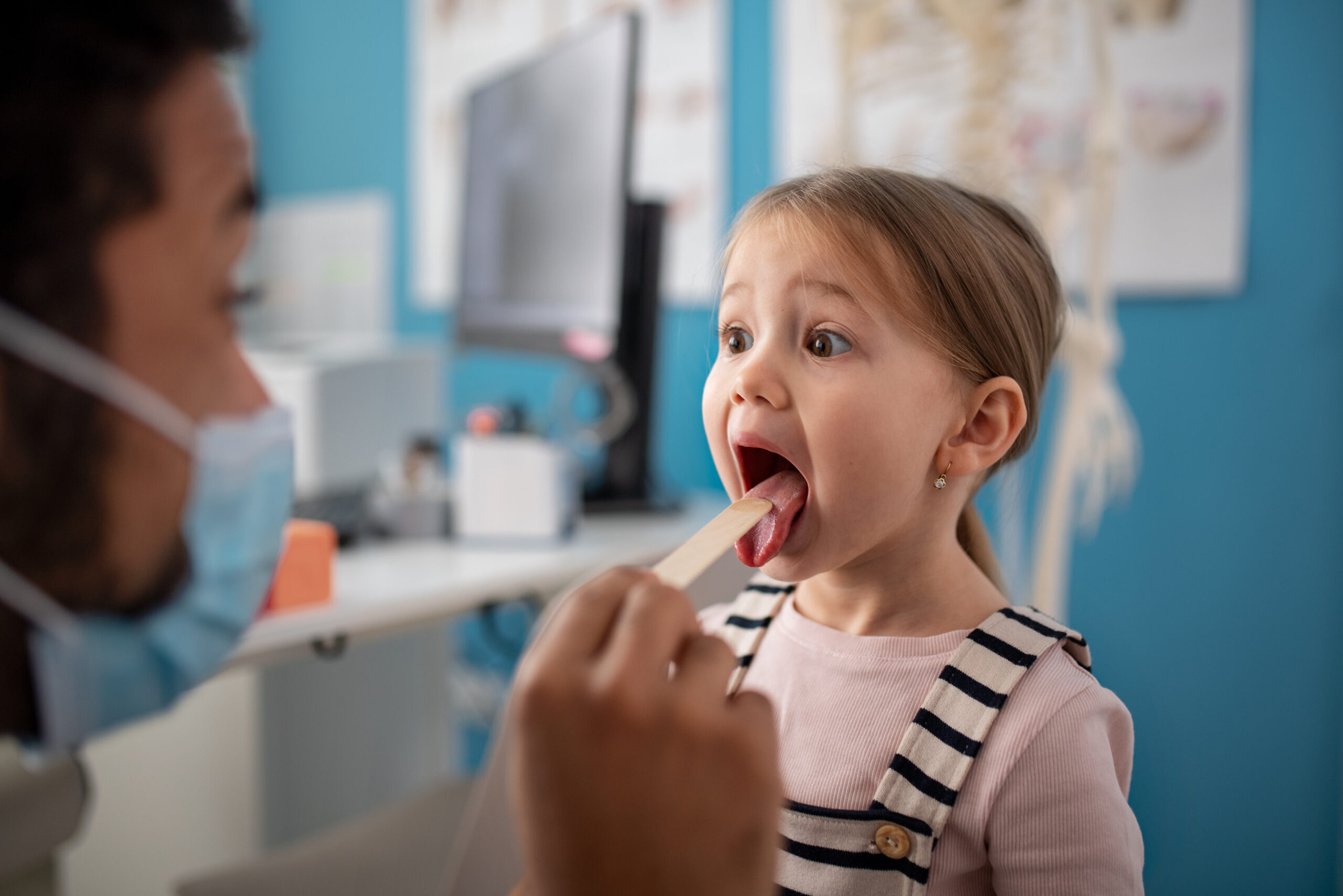 Young girl with open mouth during pediatric dental exam with tongue depressor.