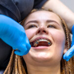 Dentist examining patient's metal braces during orthodontic treatment appointment.
