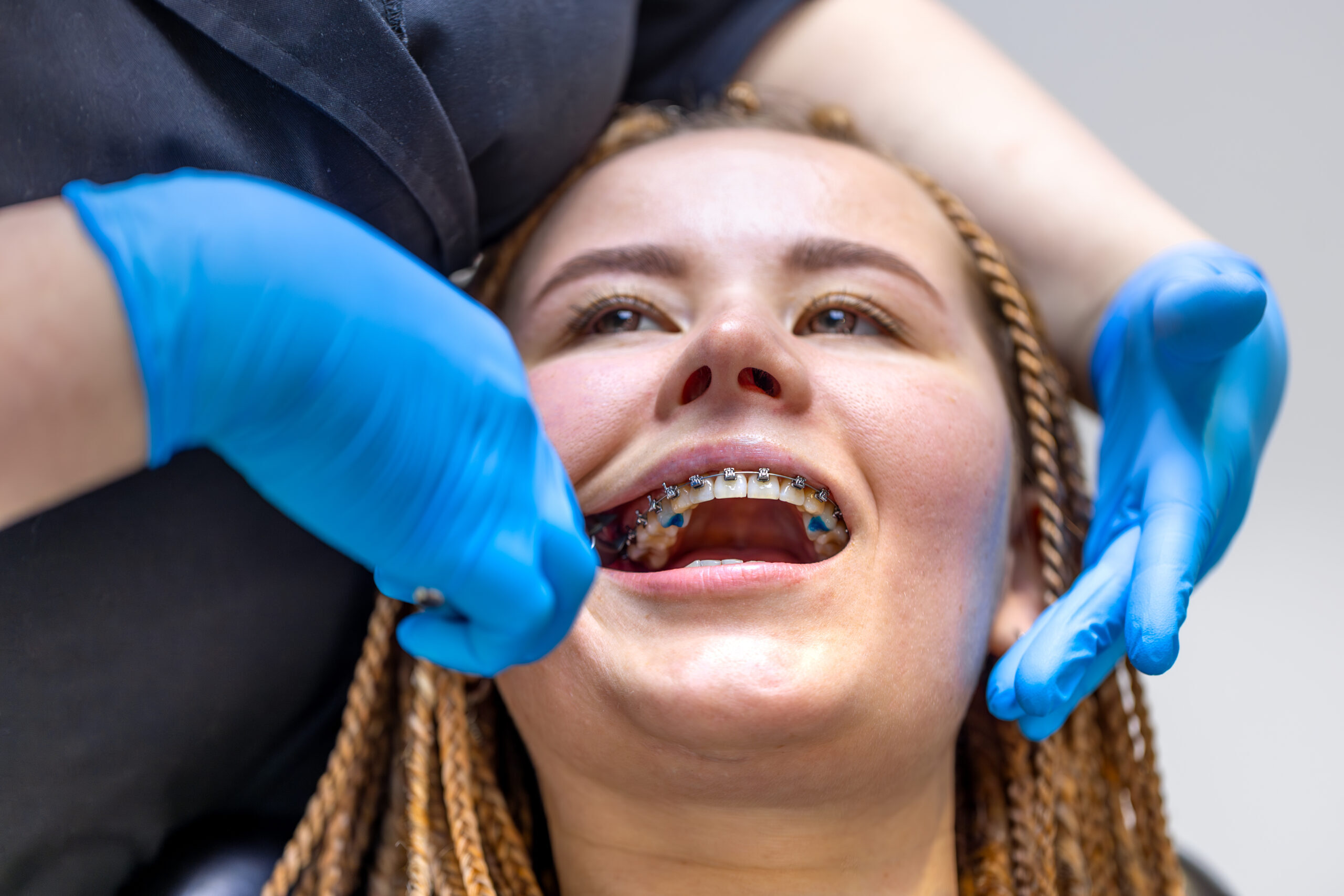 Dentist examining patient's metal braces during orthodontic treatment appointment.