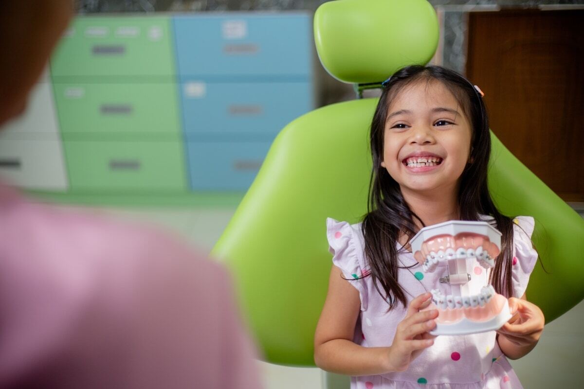 Happy child holding dental model with braces in orthodontist chair at Spring dental office.