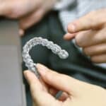 Close-up of clear aligner held by hands showing transparent orthodontic treatment option.