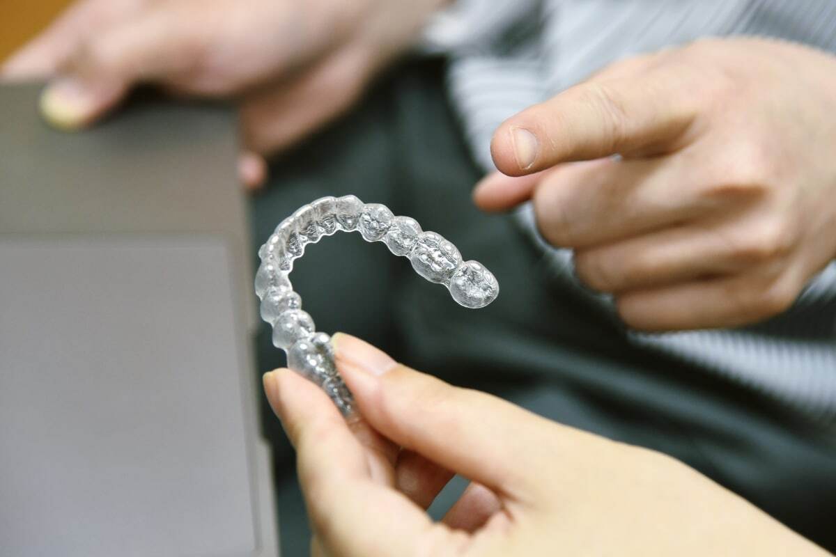 Close-up of clear aligner held by hands showing transparent orthodontic treatment option.