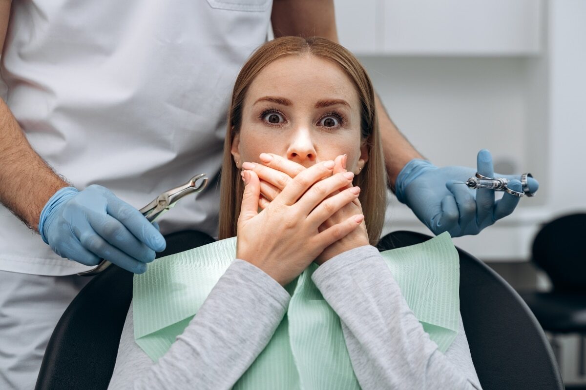 Anxious patient covering mouth during dental examination with dentist holding tools.