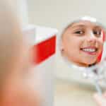 Child smiling at mirror wearing Santa hat showing healthy teeth and smile.