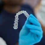 Clear Invisalign aligner held in gloved hand, showing proper orthodontic treatment device.