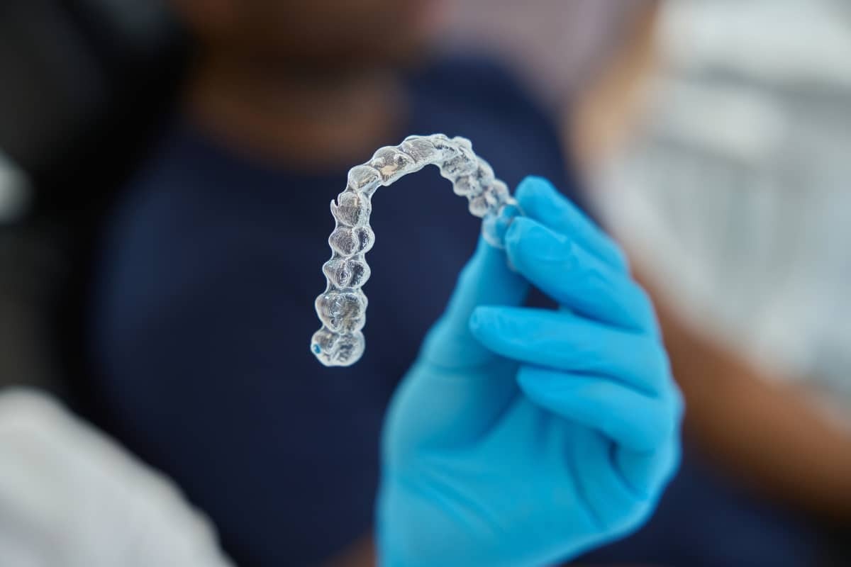 Clear Invisalign aligner held in gloved hand, showing proper orthodontic treatment device.
