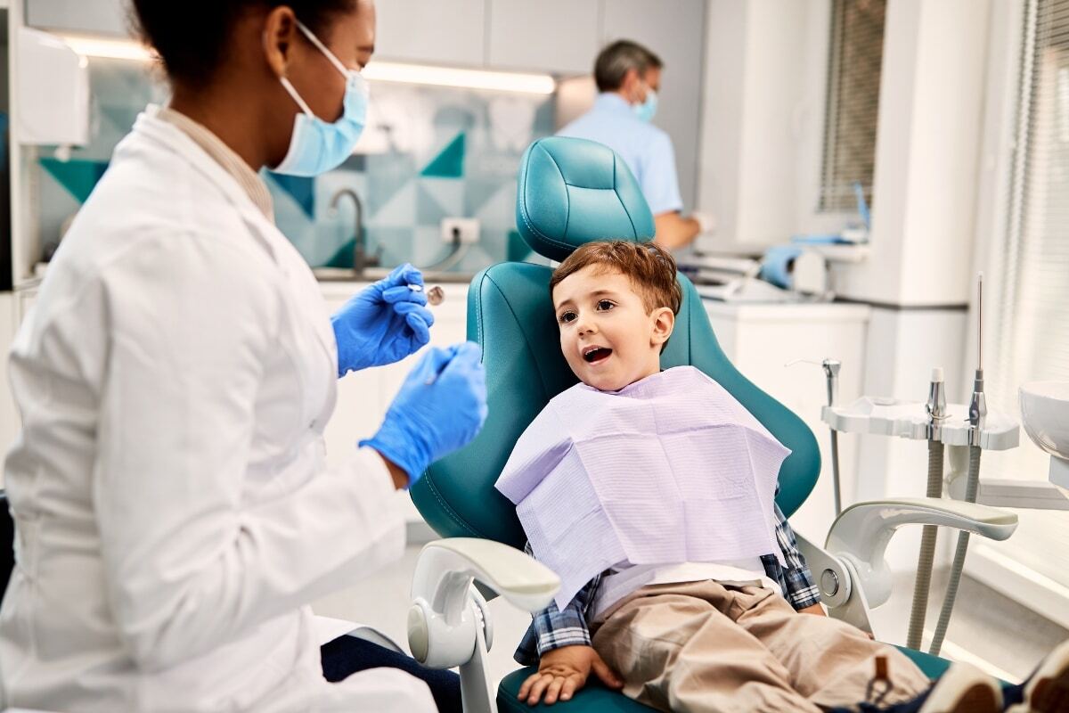 Young boy smiles in dental chair while pediatric dentist prepares for examination in Spring.