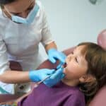 Pediatric dentist examining a child during baby tooth root canal treatment